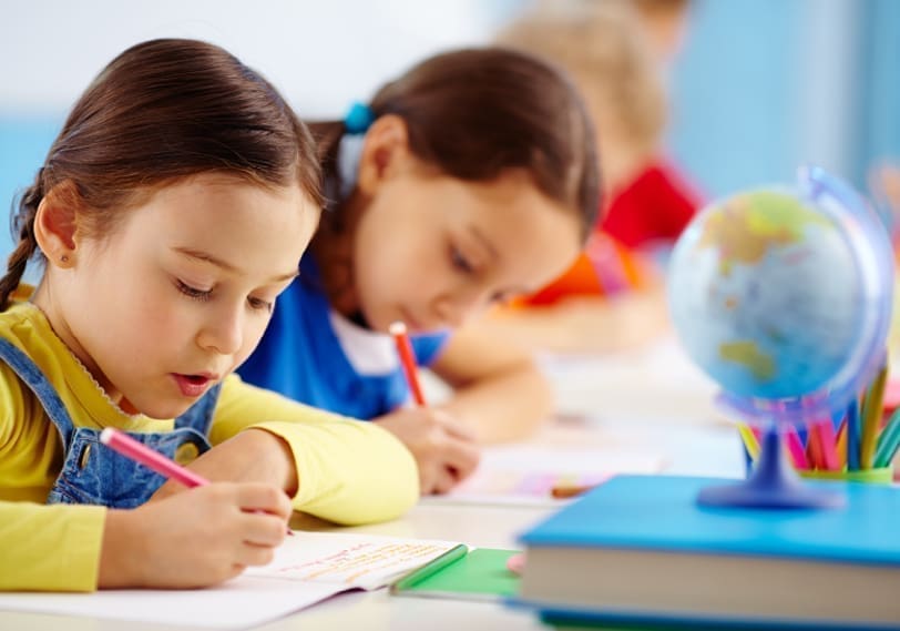 Young students writing in a classroom with a globe on the desk at KidAble.